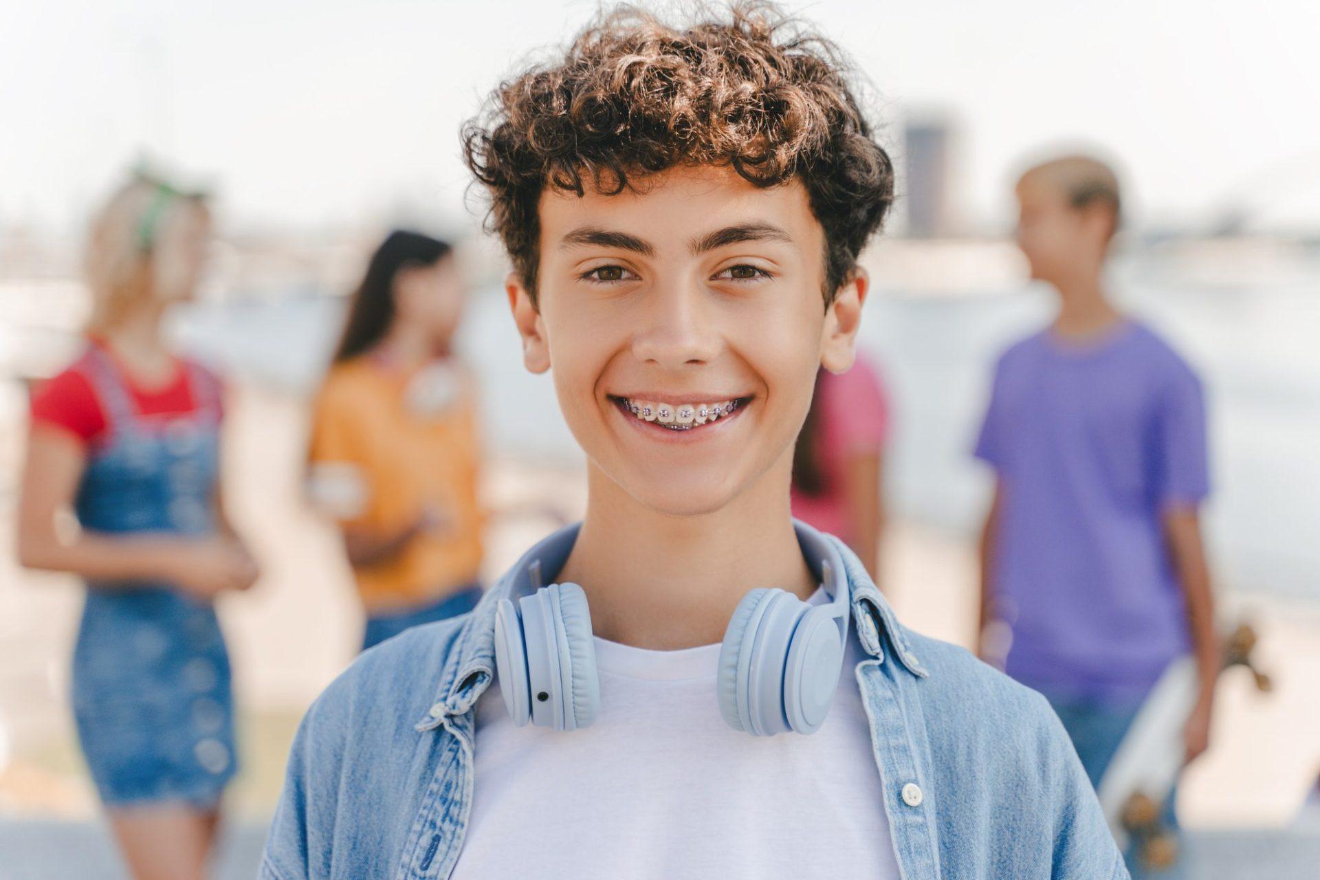 portrait of smiling teenage boy with braces wearing headphones looking at camera on the street portrait of smiling teenage boy with braces wearing headphones looking at camera on the street