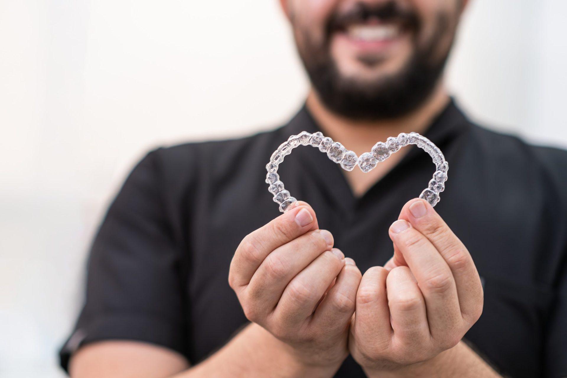 smiling doctor holding heart made of clear aligners for professional teeth correction in clinic smiling doctor holding heart made of clear aligners for professional teeth correction in clinic