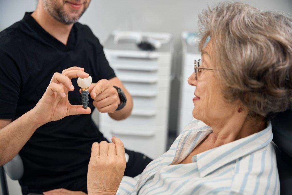 patient examines model of dental implant in hands of dental prosthetist